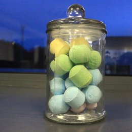 Large classic clear glass candy jar filled with colorful round pom pom candies in pastel shades of yellow, green, blue, and pink.