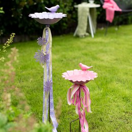  Decorative garden stakes with flower-shaped bird baths in cream, light orange, pink, and lavender colors. The stakes feature a rustic, weathered appearance and are suitable for use in outdoor garden settings.