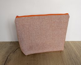Toiletry bag made of orange and beige fabric with a zipper closure.