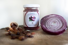 A jar of red onion compote, accompanied by sliced red onions on a wooden surface.