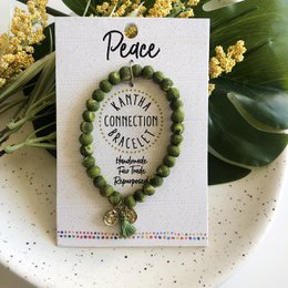  A handmade peace bracelet with a green beaded charm and the word "Peace" written on a white card.