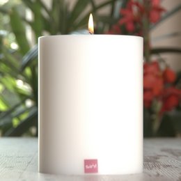 A round, white candle with a warm, flickering flame. The candle is part of a trend collection and is available in various sizes.