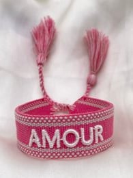 Vibrant pink charm bracelets with tassels and text designs. Includes 'Amour' and 'Good Vibes' styles in a variety of pink and red hues.