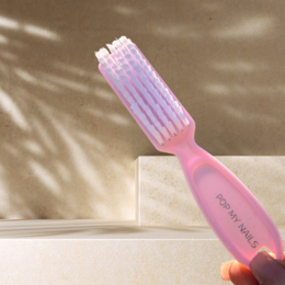  A pink nail brush with a textured bristle surface and a handle. The brush is designed for grooming and cleaning nails.