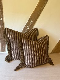 Decorative cushion with a striped pattern in shades of brown and beige, featuring tasseled edges. Suitable for living room or bedroom decor.