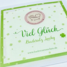 "Relaxing bath salts with a lucky clover design, made with natural ingredients like sea salt and essential oils. The bath salts have a green and white color scheme and are labeled as 'Viel Glück' or 'Good Luck'."