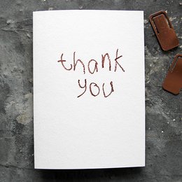 A hand-foiled greeting card with the text "thank you" written in a cursive style.