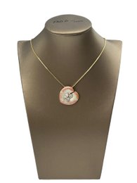 Delicate gold-tone necklace with a round pendant featuring a white flower design. Matching stud earrings included.