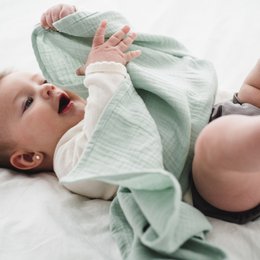 Organic cotton muslin swaddle in ocean, natural, argile, pink, and curry colors. Soft, breathable fabric perfect for swaddling newborns.