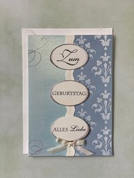 Folded birthday card with envelope featuring a floral pattern and text elements in German, including "Zum Geburtstag" (Happy Birthday).