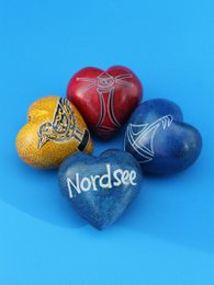Small heart-shaped soapstone statues in various colors including blue, orange, and green. The statues feature the text "Nord-see" printed on them.