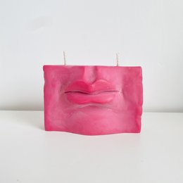 A tall, round, deep rose-colored candle with a pout-shaped design.