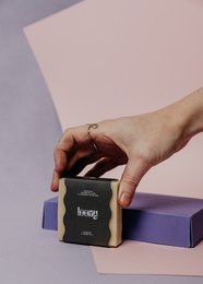 Solid shampoo bar in a black and purple packaging. The shampoo bar is made of natural ingredients and is suitable for all hair types.