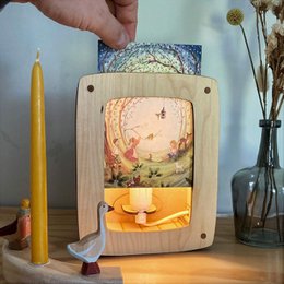  A wooden lamp with a nature-inspired design, featuring a warm-toned landscape scene with a sun, trees, and a yellow candle.