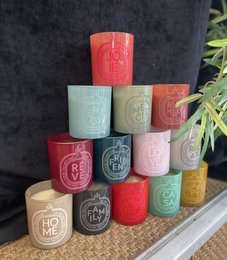 Colorful scented candles in various shapes and sizes, including round and tall candles with text and patterns.