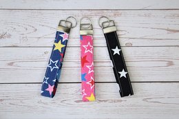 Handmade key fobs in a variety of colorful star and animal designs, including butterfly, dinosaur, pink star, blue star, gold bee, grey bee, pink bee, leopard print, small black star, and large black star. These key fobs are perfect as gifts for women and men.