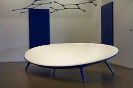 A modern, low-profile sofa with a white oval-shaped seat and blue metal frame. The sofa has a minimalist, contemporary design that would suit a variety of living spaces.