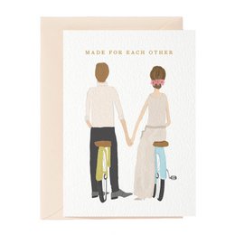 A wedding card featuring an illustration of a couple holding hands, with the text "Made For Each Other" above them. The card has a warm, neutral color palette and a simple, minimalist design.