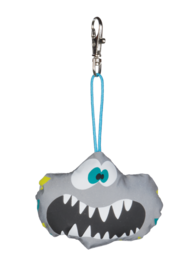A gray and blue monster-shaped keychain with large teeth and a zipper-like mouth. The keychain has a light blue strap for attaching to bags or clothing.
