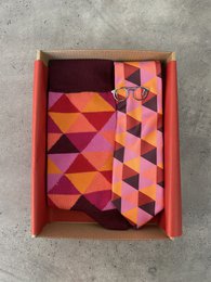 This set includes a tie, socks, and a tie bar in a magenta rhombus pattern. The tie, socks, and tie bar are made of high-quality materials and feature a stylish geometric design in shades of pink, purple, and orange.