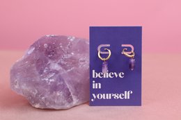 "Elegant drop earrings with the message 'Believe in Yourself' printed on a purple card. The earrings feature a simple, minimalist design with a silver-tone finish."
