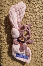 A soft, plush teething ring in the shape of a turtle, with a purple body and pink cloth accents. Designed to soothe a baby's gums during the teething process.
