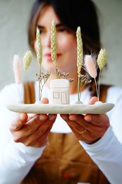 A small decorative house surrounded by tall, wispy grass-like plants in a natural, minimalist style.