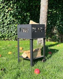 A modern, rectangular fire pit made of black metal with a sleek, minimalist design. The fire pit is surrounded by dry grass and plants, creating a natural and rustic ambiance.
