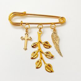 A gold-colored pin with charms including a cross, leaves, and a feather. This pin is suitable as a gift for a birth or christening.