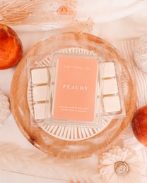 Peach-scented wax melts, warm peachy orange color, square individual pieces, decorative packaging with text label.