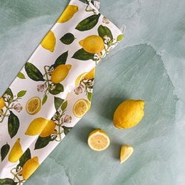 Organic tea towel with a lemon print pattern, featuring vibrant yellow lemons and green leaves on a white background.