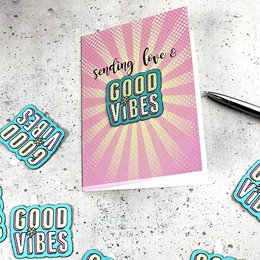 A greeting card with a pink and yellow background featuring the text "Sending love & good vibes" in a retro-style font. The image also includes a sticker-patch design with the text "GOOD VIBES" in a colorful, embroidered style.