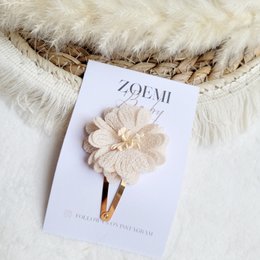 A large, beige flower-shaped hair clip with a textured, layered design and a pearl-like center.