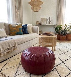  A round, burgundy leather pouffe with a decorative stitched pattern. The pouffe appears to be stuffed and has a plush, comfortable look.