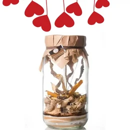A glass jar containing a brown liquid and various spices, including vanilla beans and citrus peels. The jar is decorated with red heart-shaped ornaments hanging above it.
