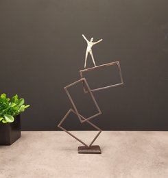 Metallic abstract statue of a figure balancing on geometric shapes, with a minimalist, modern design.
