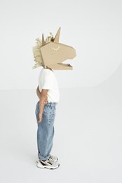 Cardboard unicorn mask, DIY arts and crafts project. Includes a person wearing the mask, which appears to be made of cardboard and has a horn and ears. The mask has a whimsical, playful design.
