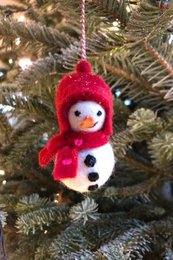 A plush snowman ornament with a red hat and scarf, hanging on a Christmas tree.