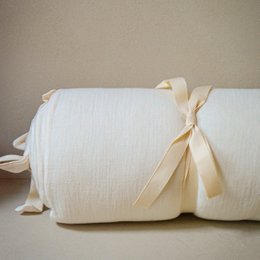 Cream-colored bed/playpen bumper made of soft, plush material with a bow accent.