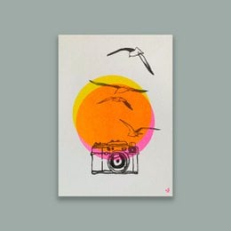 Art print featuring a camera silhouette against a vibrant orange sun and abstract landscape elements.