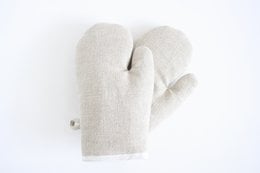 Pair of linen oven gloves, off-white in color, with a simple, minimalist design. Suitable for protecting hands while handling hot items in the kitchen.