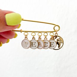 Gold-toned safety pin charm with the word "PEACE" and peace symbol charms.