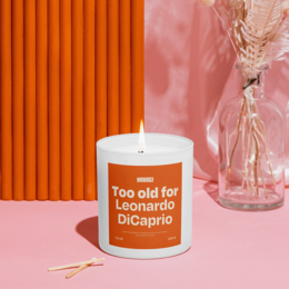 Tall, round, orange scented candle with the text "Too old for Leonardo DiCaprio" printed on the label.