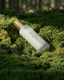 "Clear glass bottle with gold cap, green text label, lightweight serum packaging, minimalist skincare design"