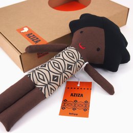 A plush African-inspired doll with a black body, patterned fabric, and a tag. The doll appears to be a baby or child's toy.
