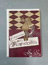 Folded Christmas card with envelope featuring a festive reindeer design in shades of burgundy and gold. The card has a "Merry Christmas" message.