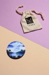 Lilac-colored pocket mirror with a reflective surface and a drawstring pouch.