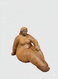 A cast iron garden sculpture depicting a seated female figure with a rounded, voluptuous shape and a textured, earthy finish.