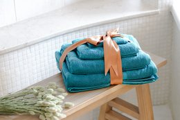 Soft, plush teal blue towels in a bathroom setting. The towels appear to be made of a high-quality, absorbent material and are neatly stacked on a wooden shelf.