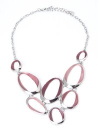 A rhodium-plated metal necklace with a statement design featuring a bib-style arrangement of oval-shaped links in a mix of silver and pink tones.
